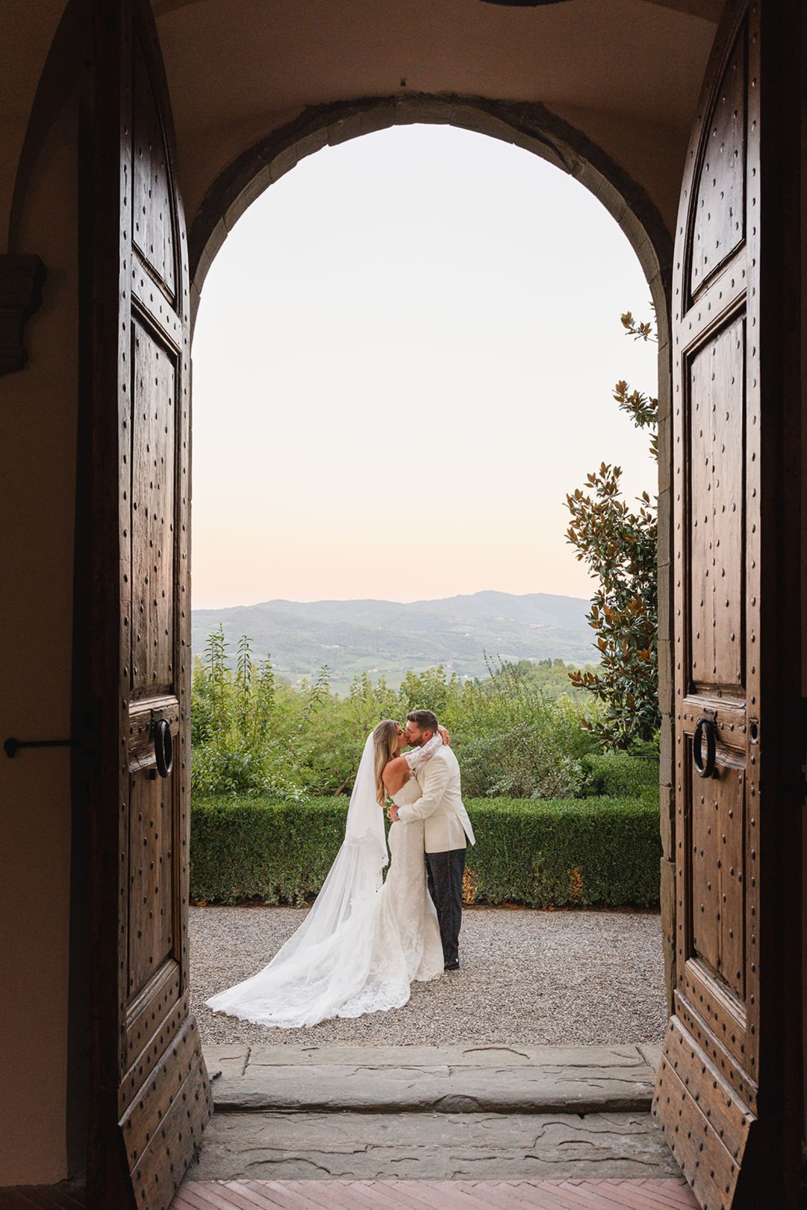 A bride and groom kiss framed by the arches of Castello Vicchiomaggio
