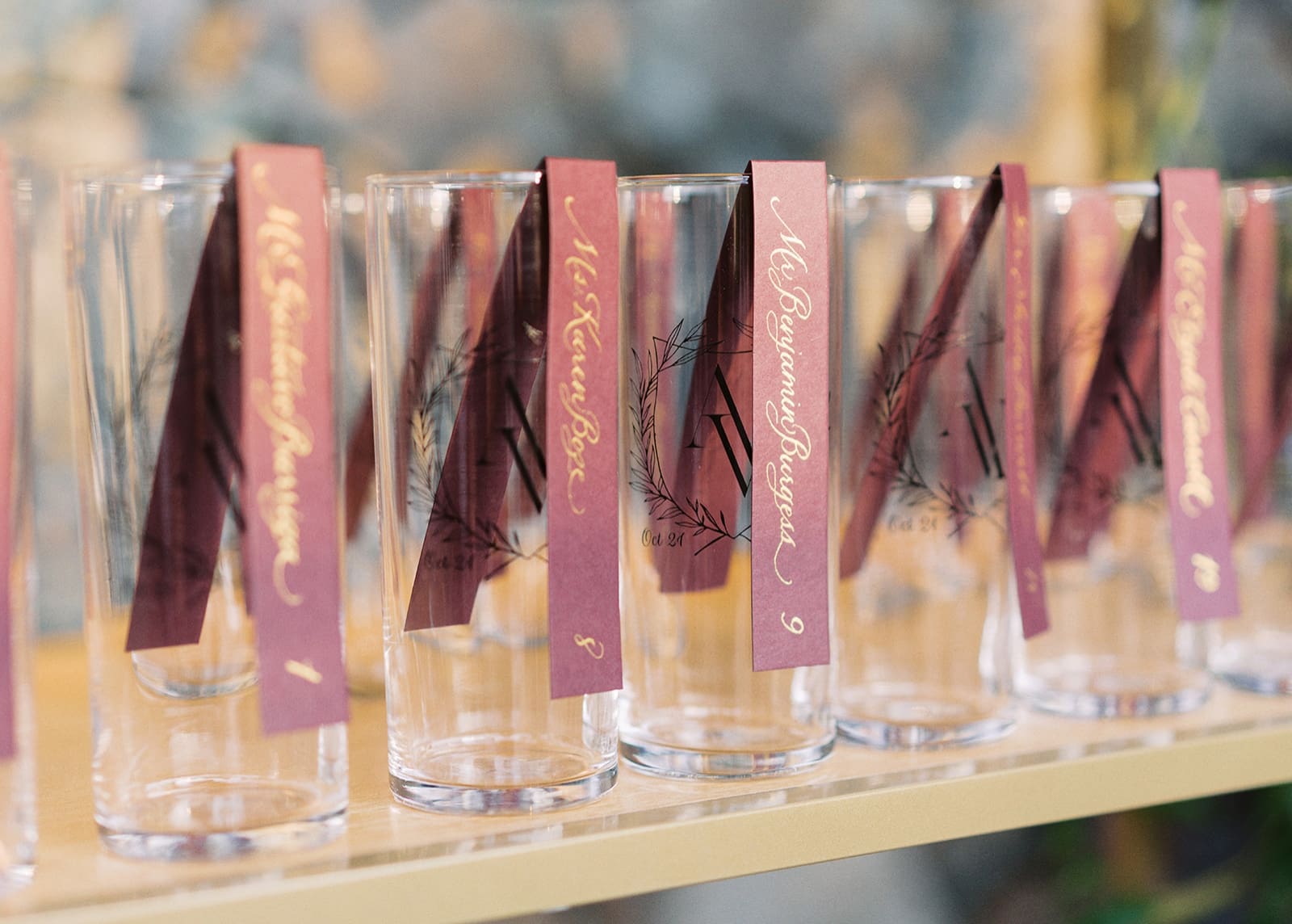 A seating chart of tall glasses with guest's names in gold calligraphy on purple paper folded inside